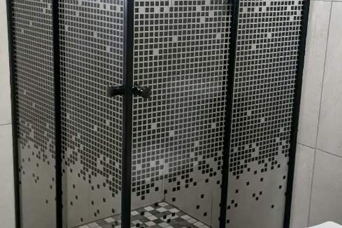 Modern bathroom featuring a corner shower enclosure with a black frame, rain shower head, and a white toilet with tiled finishes.