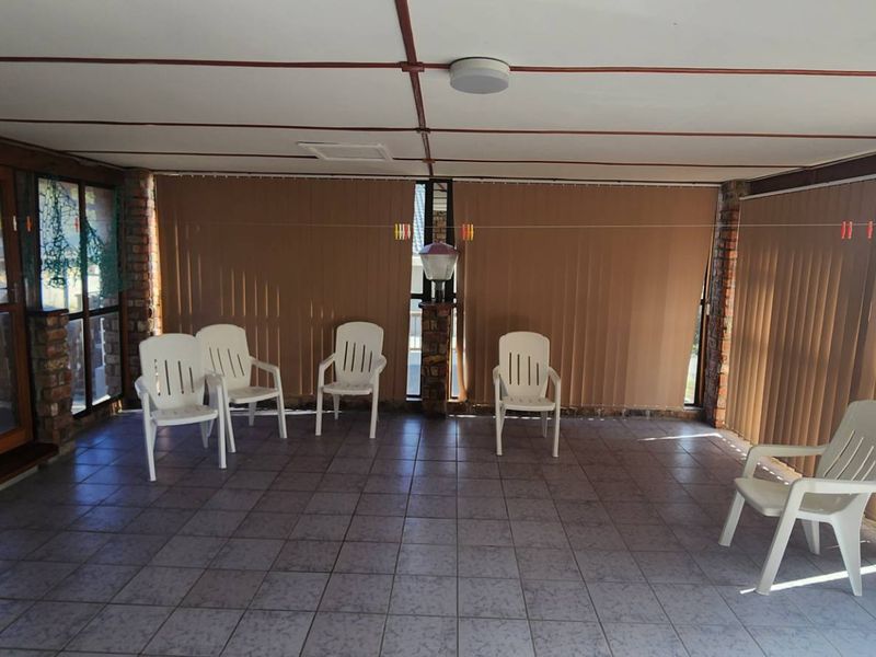 A covered patio area featuring exposed brick pillars, tiled flooring, and vertical blinds, providing a functional outdoor living space.