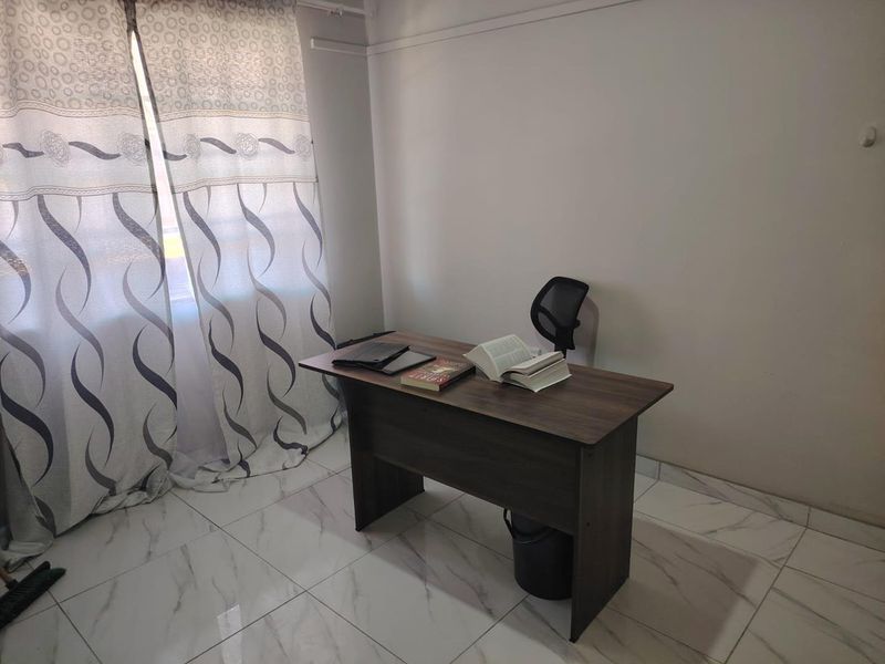 A functional office space featuring modern marble-look floor tiles and natural light through window curtains.