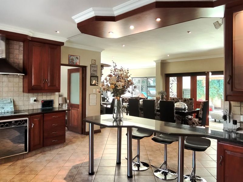 Spacious open-plan kitchen featuring rich wooden cabinetry, granite countertops, a breakfast bar, and integrated appliances, flowing seamlessly into the dining and living areas.