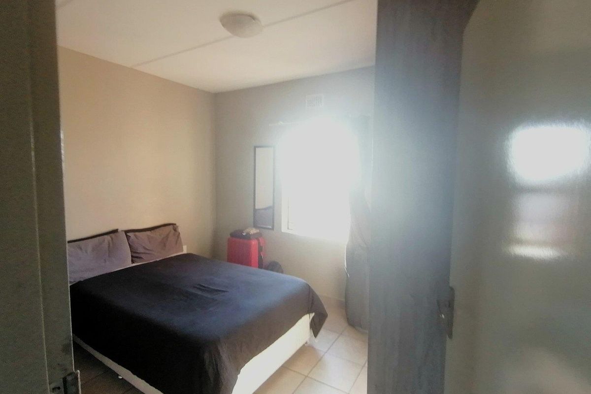 A standard bedroom featuring tiled flooring and a window, viewed from the doorway.