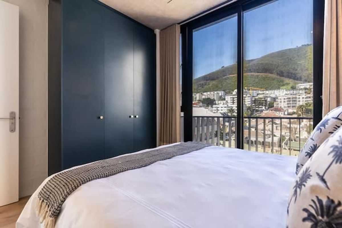 A modern bedroom featuring dark blue built-in cupboards, laminate flooring, and a large sliding glass door opening to a balcony with mountain views.