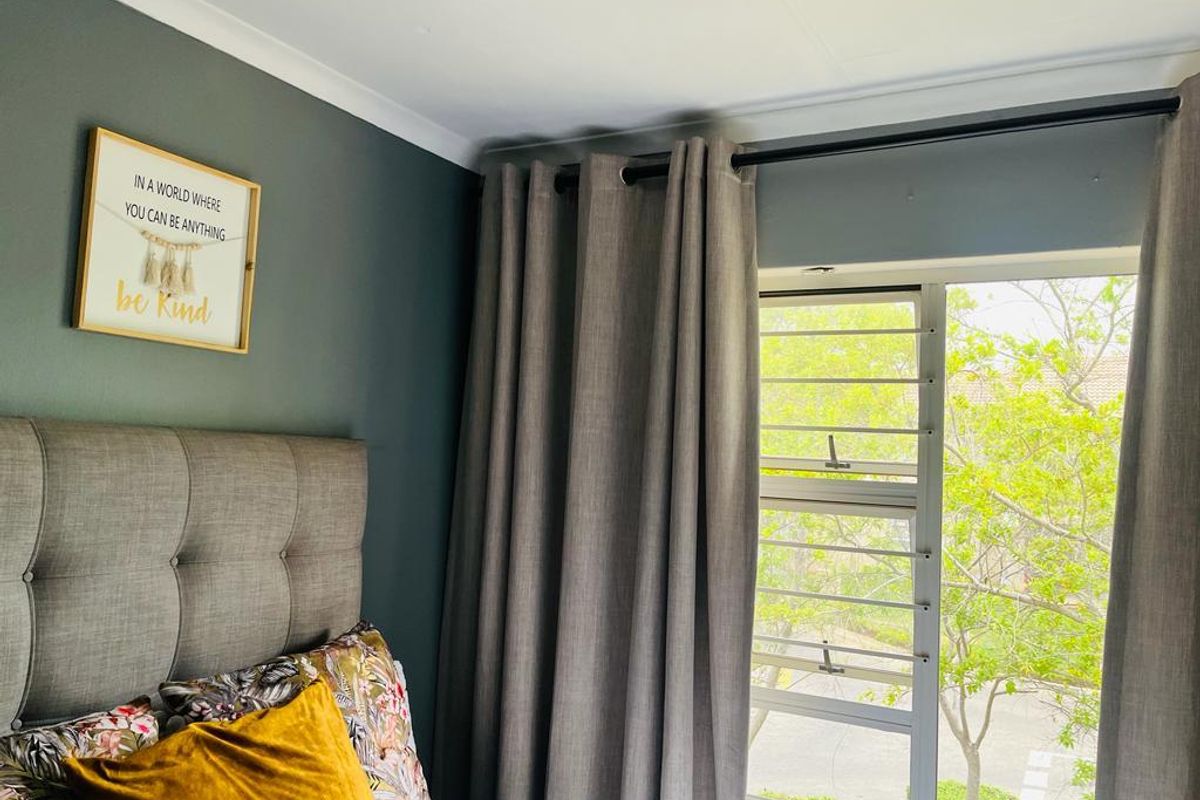 A bedroom featuring a dark accent wall, a large window with security bars, and neutral curtains.