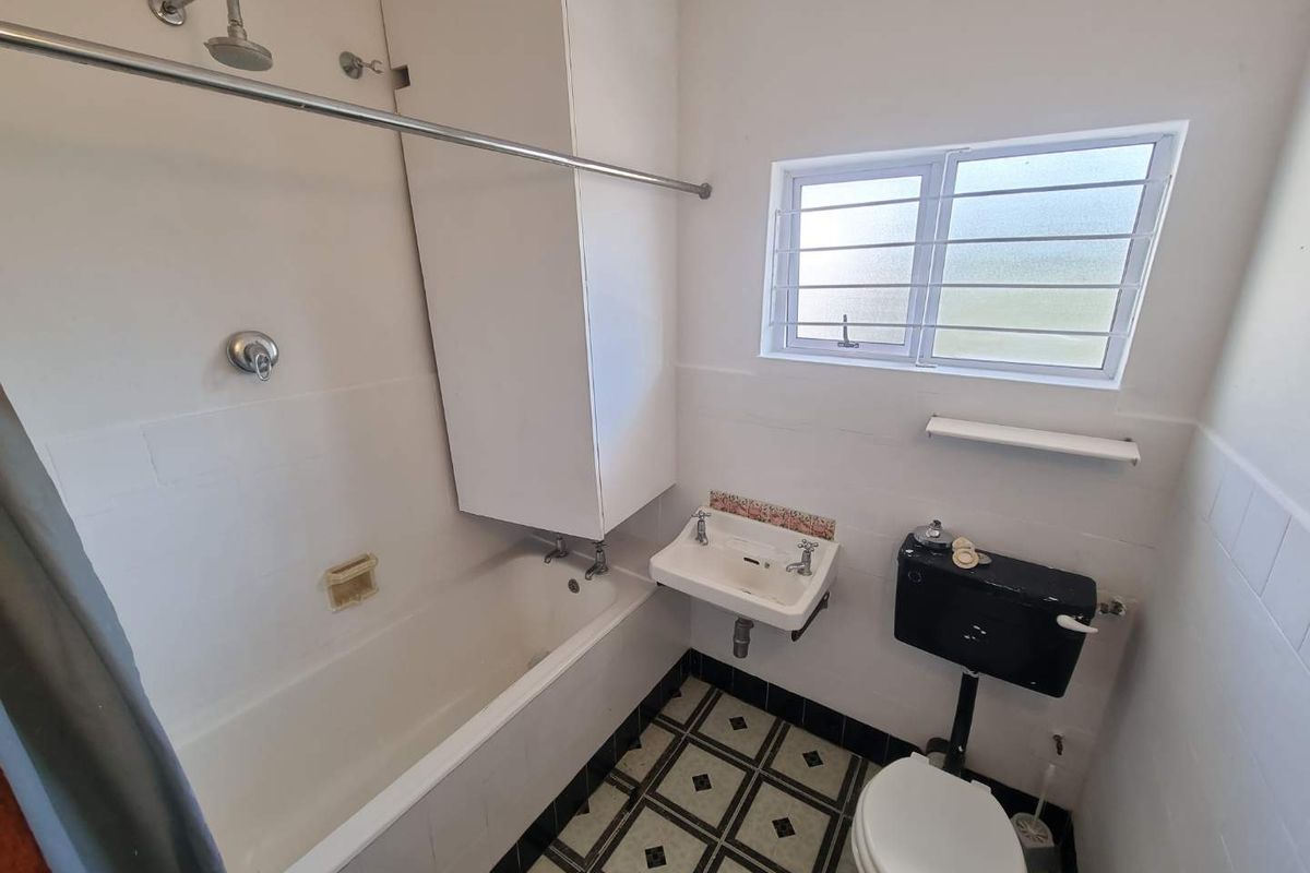 A dated bathroom featuring a bathtub with shower attachment, wall-mounted basin, and a traditional high-level cistern toilet, requiring modernization of finishes and fixtures.