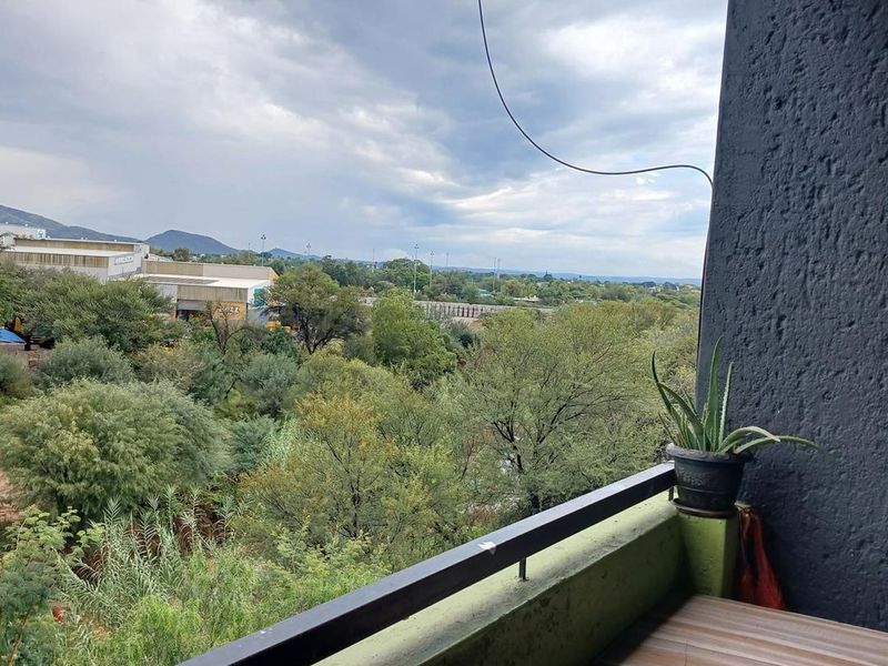 A balcony featuring a metal railing and textured wall finish, offering an elevated view of the surrounding landscape and greenery.