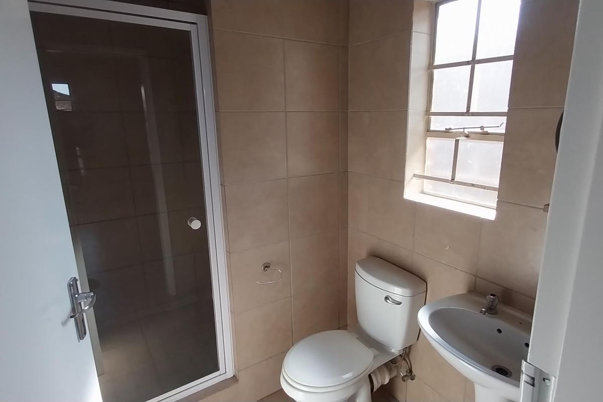 A functional bathroom featuring a shower enclosure, pedestal basin, and toilet, finished with neutral wall tiling and a window for natural light.