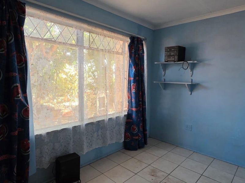 A vacant bedroom featuring tiled flooring, a large leaded glass window, and wall-mounted shelving, offering a blank canvas for renovation.