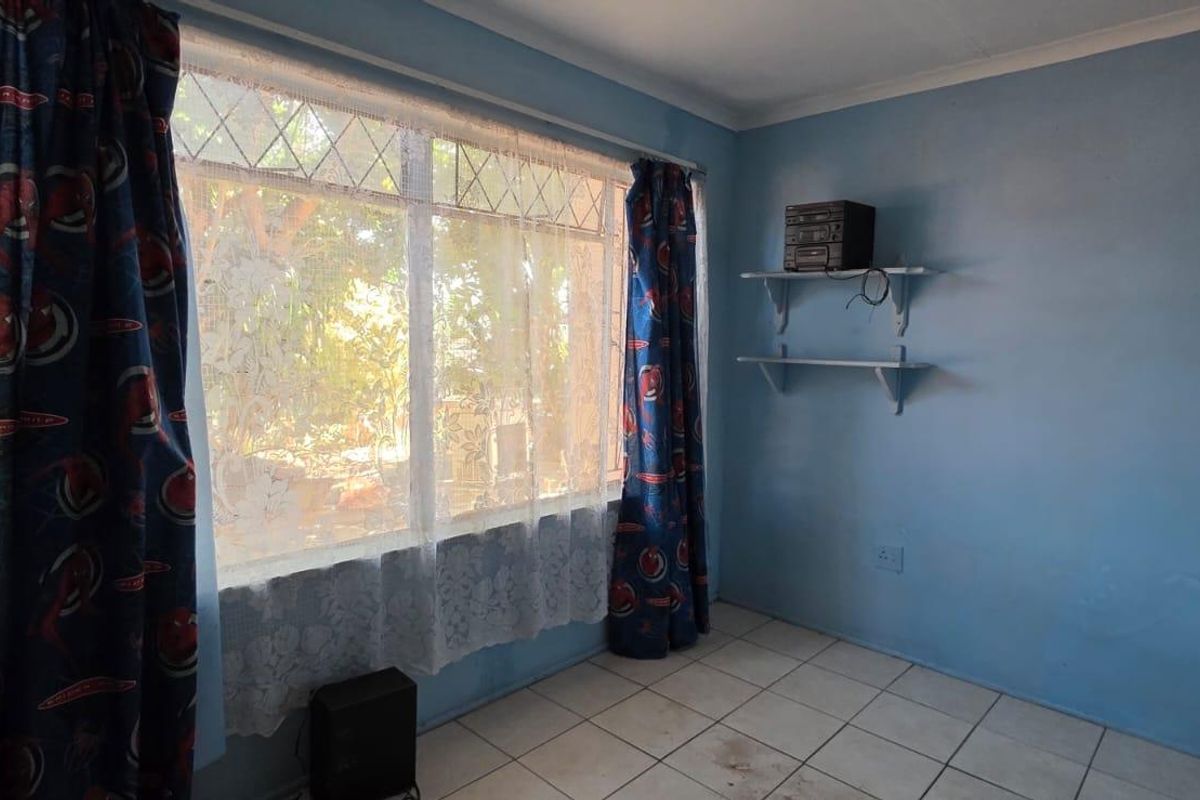 A vacant bedroom featuring tiled flooring, a large leaded glass window, and wall-mounted shelving, offering a blank canvas for renovation.