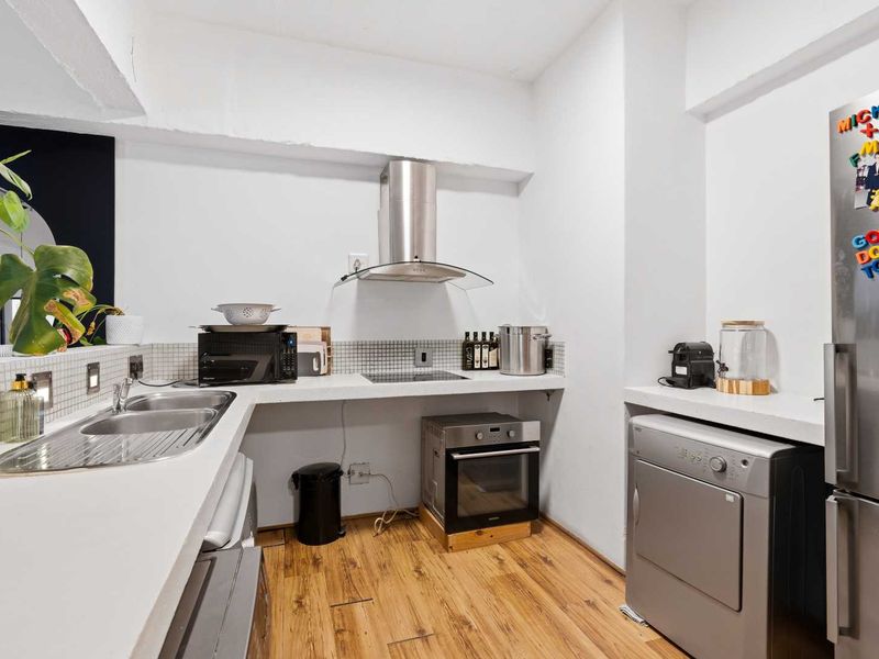 A functional kitchen area featuring a stainless steel extractor fan, built-in oven, hob, double sink, and mosaic tile backsplash with laminate flooring.
