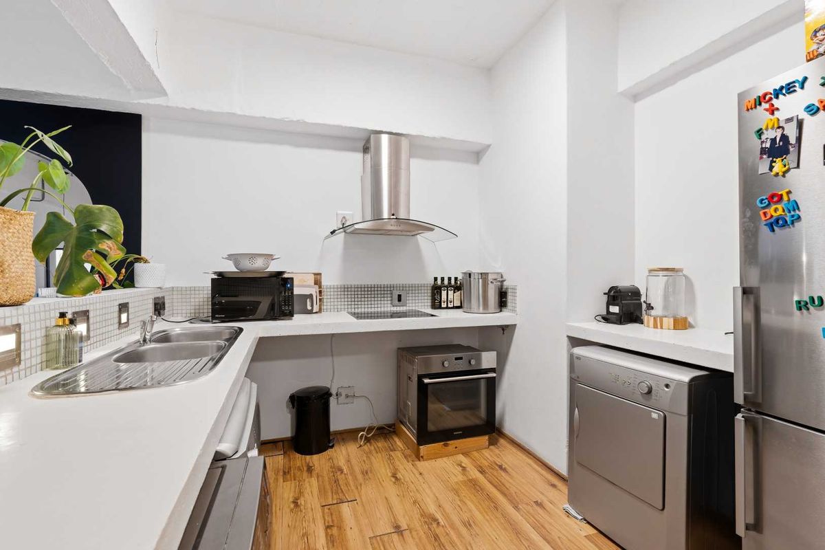A functional kitchen area featuring a stainless steel extractor fan, built-in oven, hob, double sink, and mosaic tile backsplash with laminate flooring.
