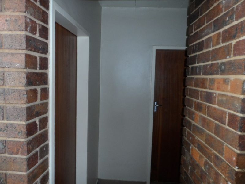 A narrow hallway featuring exposed brick wall accents and timber doors, providing access to various rooms within the apartment.