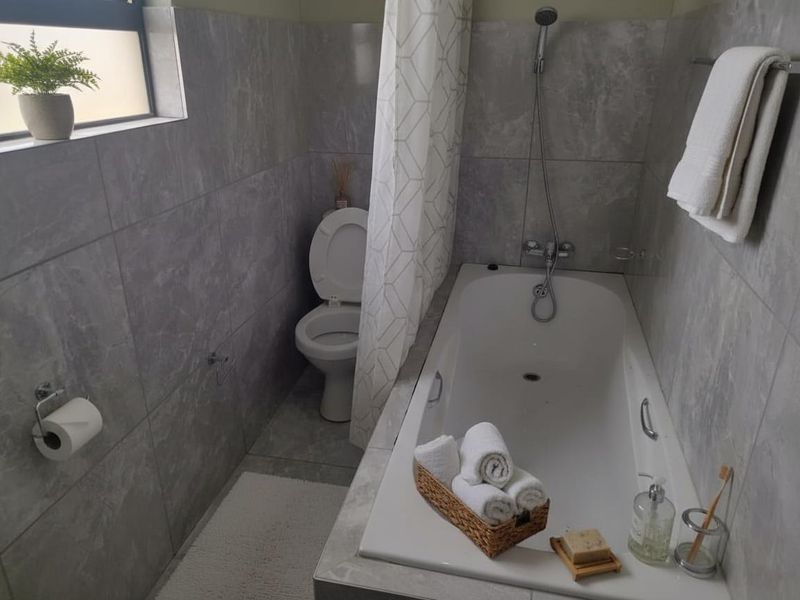 A functional bathroom featuring grey marble-look wall and floor tiles, a built-in bathtub with shower mixer, and a standard toilet.