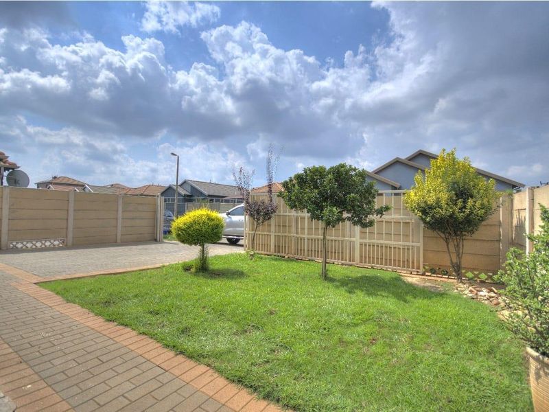 A well-maintained rear garden featuring a paved driveway, neat lawn, and secure precast concrete boundary walling.