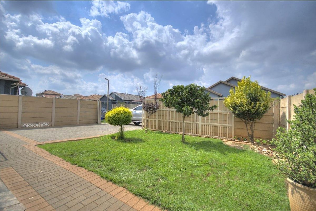 A well-maintained rear garden featuring a paved driveway, neat lawn, and secure precast concrete boundary walling.