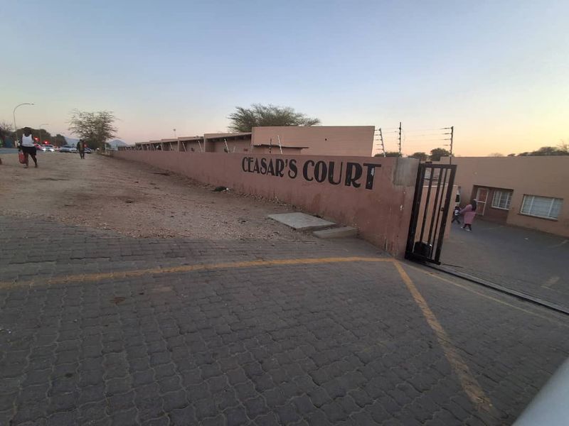 Front entrance view of Ceasar's Court townhouse complex featuring a boundary wall, electric fencing, and a paved driveway entrance.