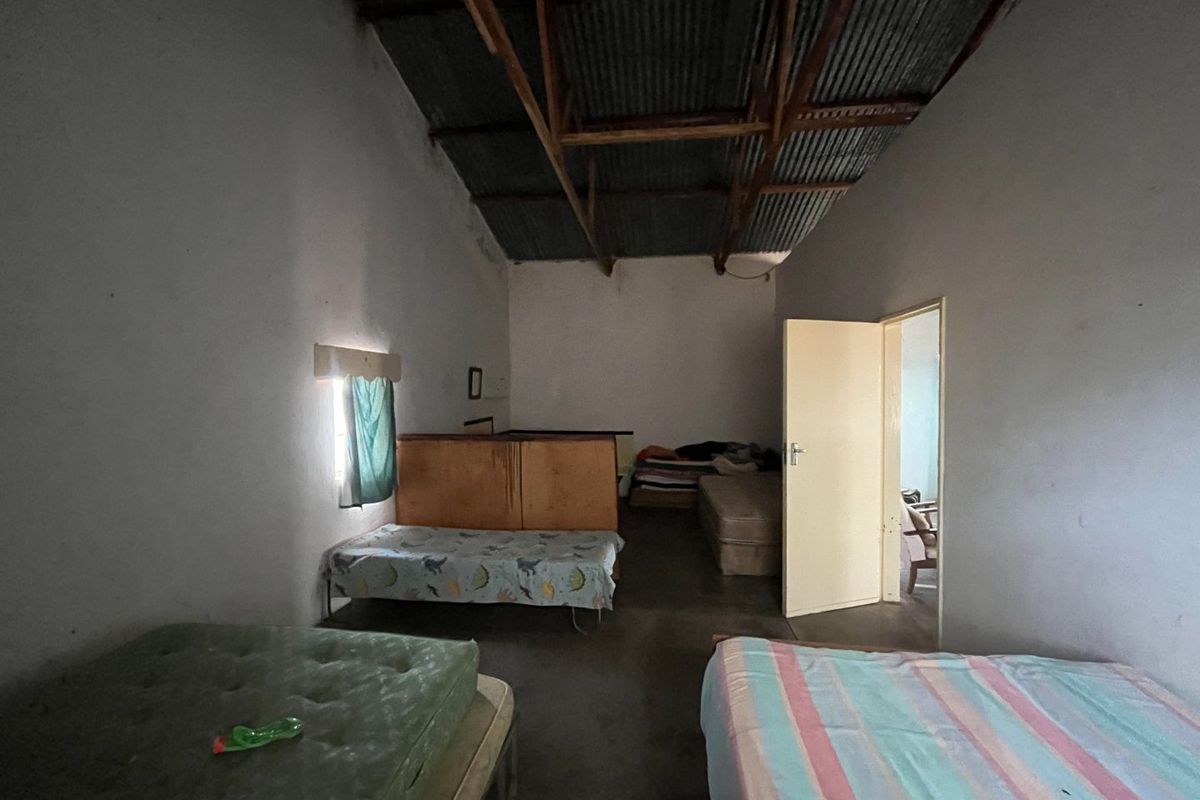 A rustic bedroom space featuring exposed corrugated metal roofing, concrete flooring, and basic interior finishes, offering a functional layout for multiple beds.