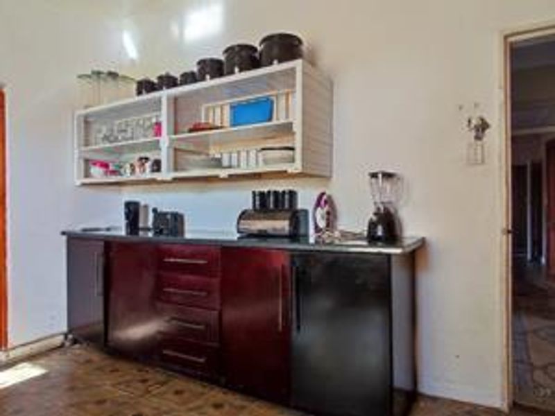 A functional kitchen area featuring dark built-in cabinetry, laminate countertops, and open wall-mounted shelving, providing basic storage and preparation space.