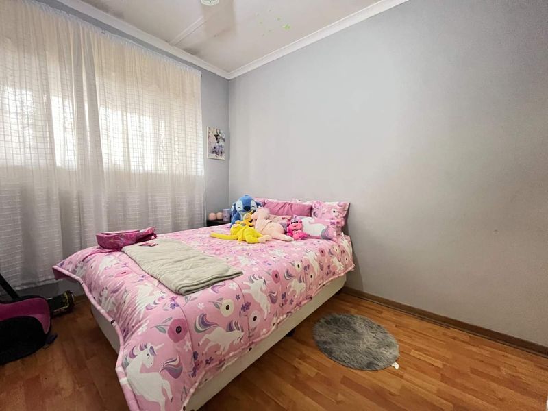 A bedroom featuring laminate flooring, neutral wall paint, and a window with curtain rails, providing a functional and well-lit living space.