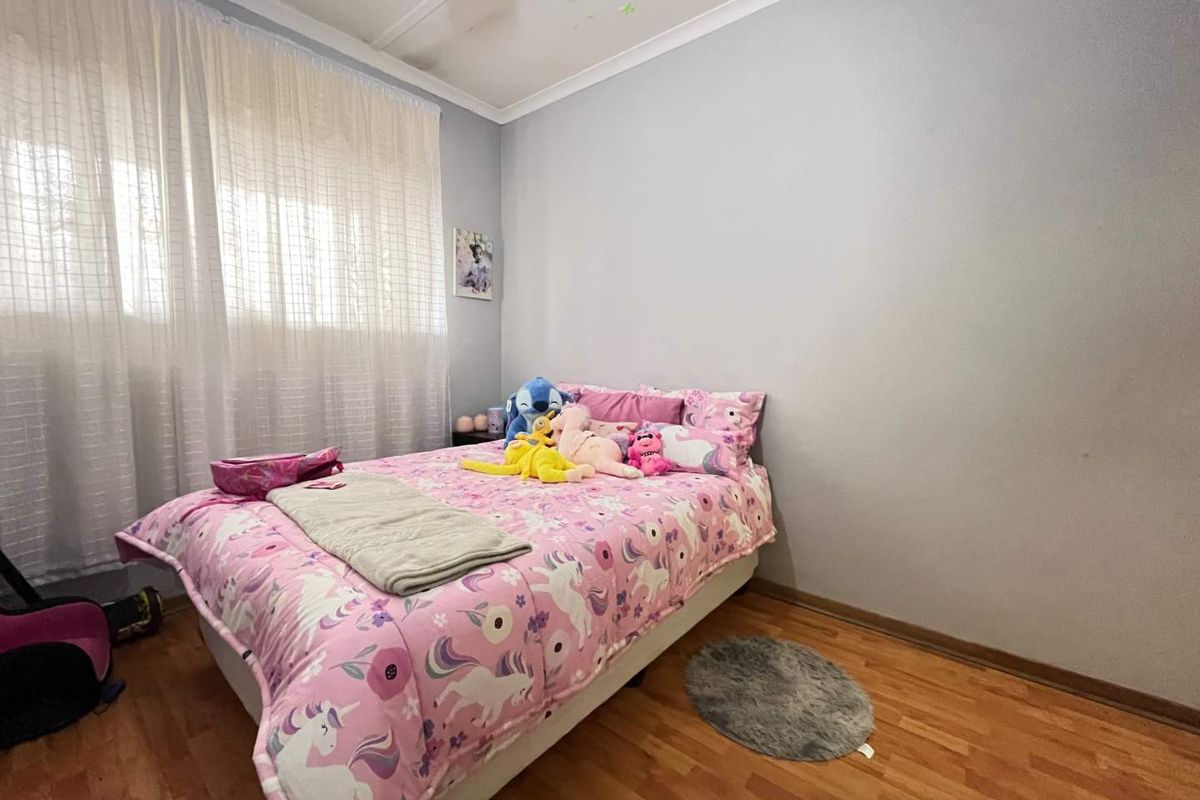 A bedroom featuring laminate flooring, neutral wall paint, and a window with curtain rails, providing a functional and well-lit living space.
