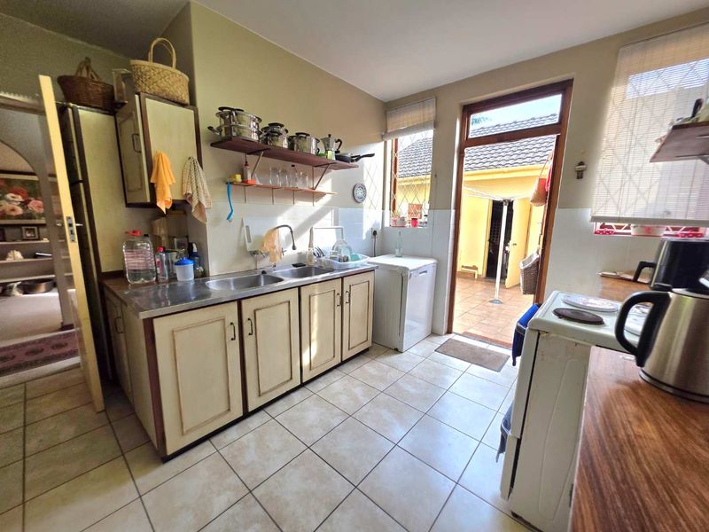 A functional kitchen featuring tiled flooring, double bowl sink, built-in cabinetry, and direct access to the rear patio area.