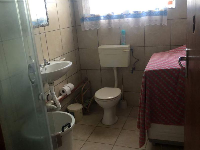 A functional bathroom featuring a pedestal basin, toilet, and shower enclosure with tiled finishes throughout, requiring some cosmetic updates.