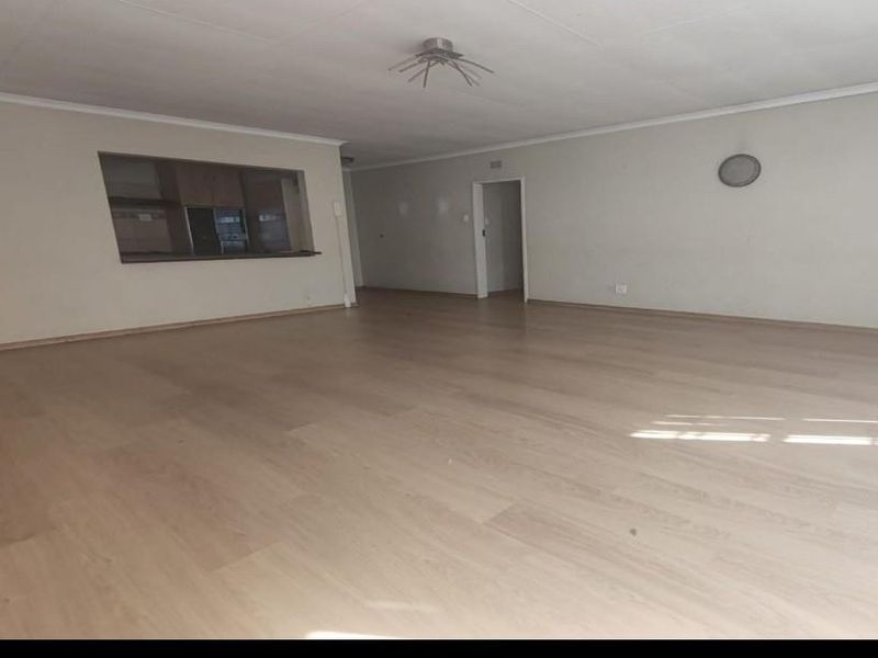 Spacious, empty open-plan living area featuring light laminate flooring and a convenient serving hatch connecting to the kitchen space.