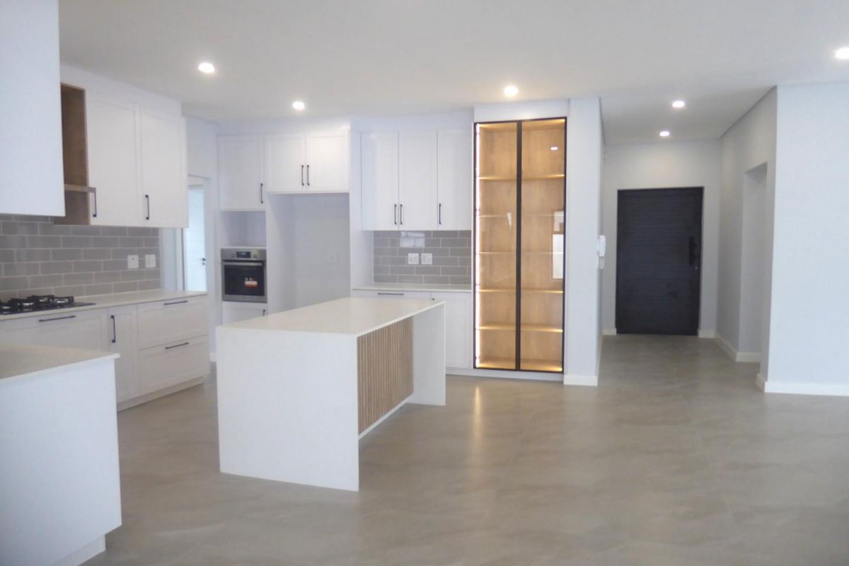 Modern, open-plan kitchen featuring white cabinetry, a central island, built-in oven, gas hob, and elegant glass-front display shelving with integrated lighting.