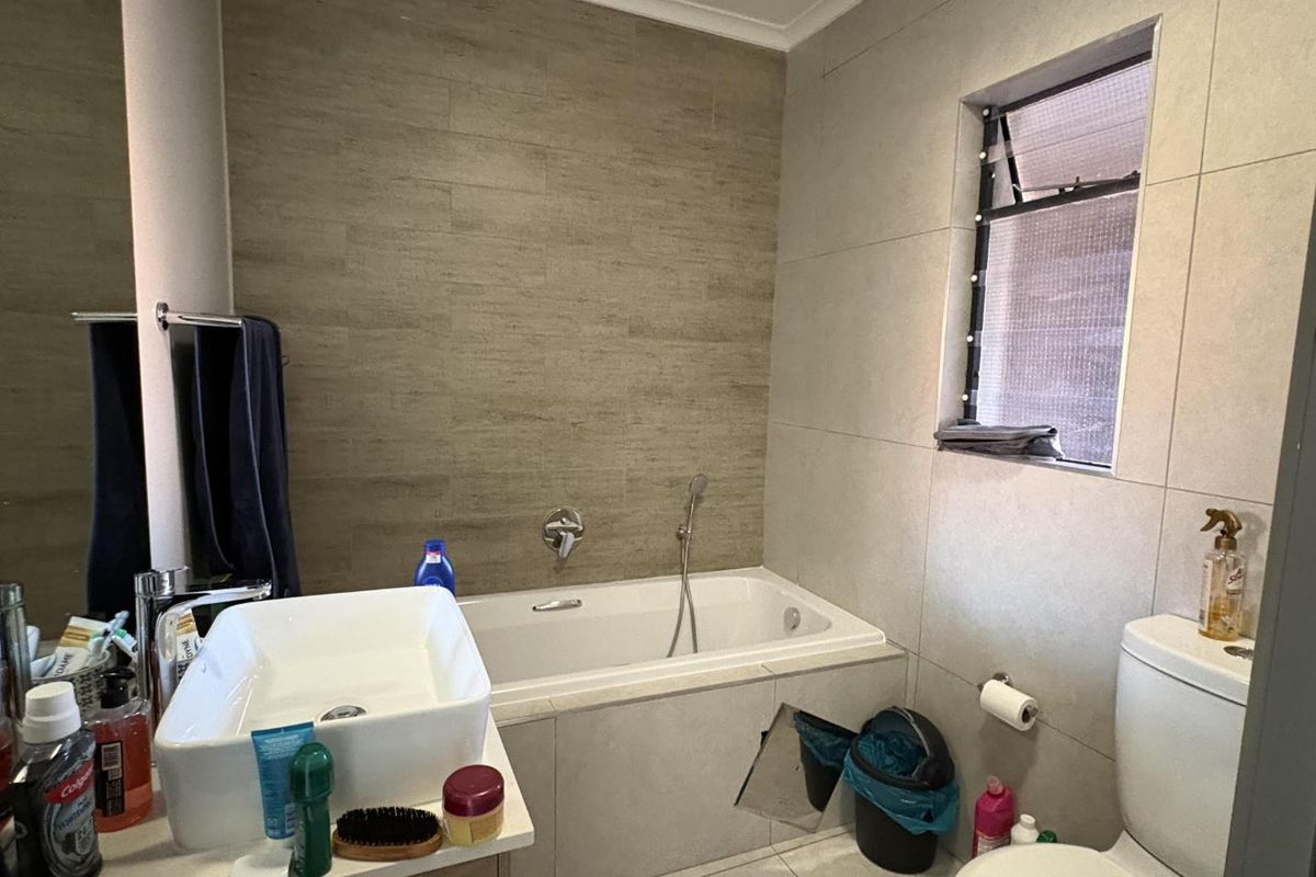 Modern bathroom featuring a built-in bathtub with shower mixer, a vessel sink vanity, and neutral wall tiling.