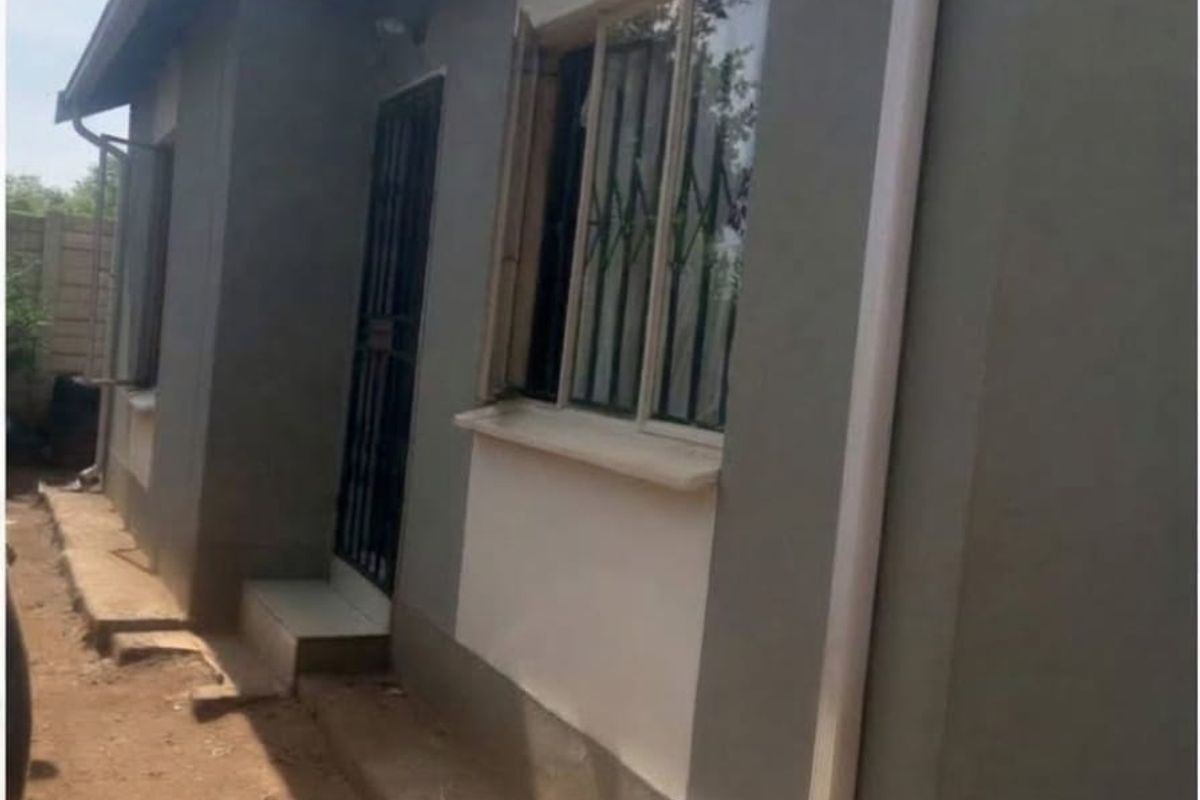 Side view of the house exterior featuring grey painted walls, white downpipes, security bars on windows, and a metal security gate at the entrance.
