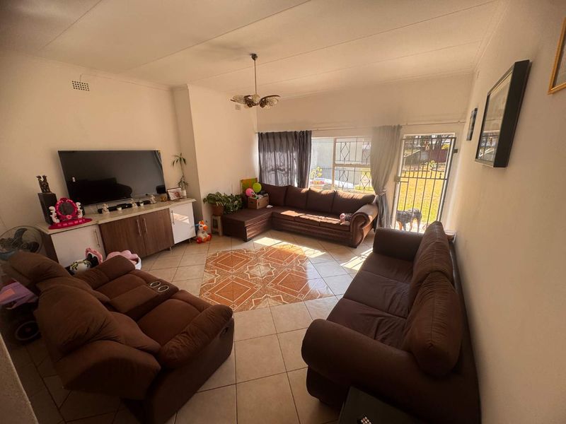 A spacious living room featuring ceramic floor tiles, a sliding glass door with security gate access to the garden, and a central ceiling light fixture.