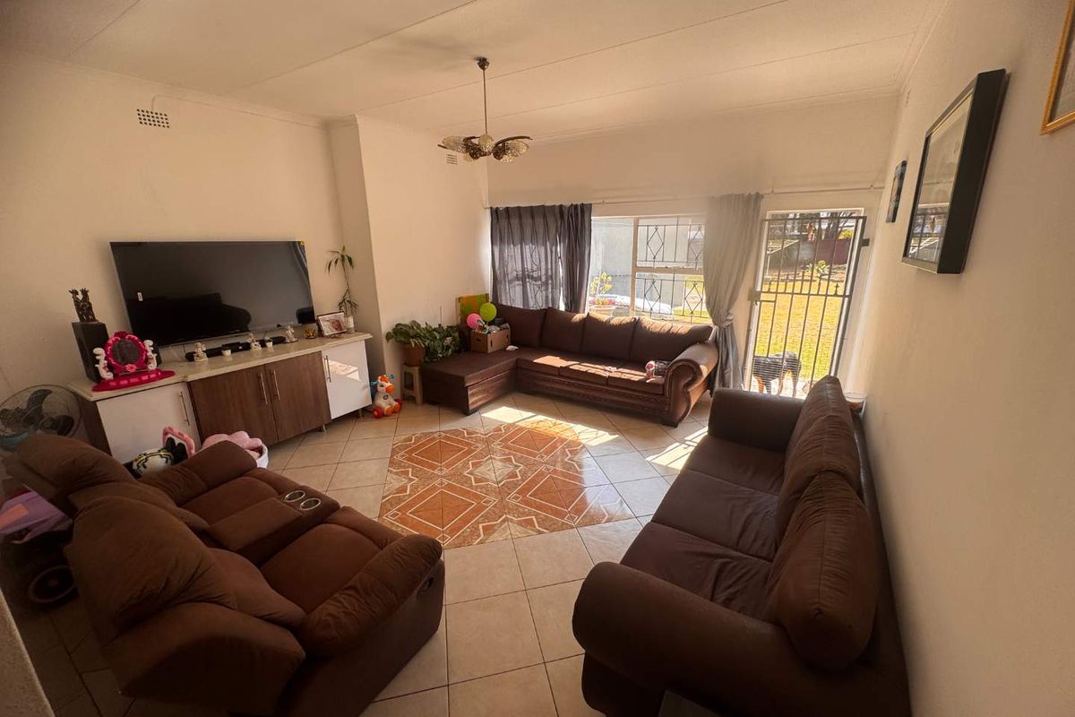 A spacious living room featuring ceramic floor tiles, a sliding glass door with security gate access to the garden, and a central ceiling light fixture.