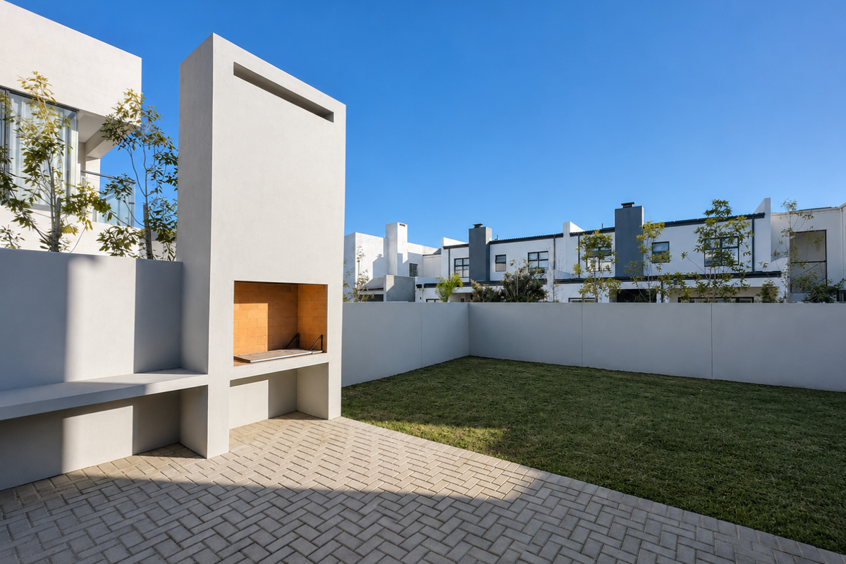 A modern rear garden featuring a paved patio area, a built-in brick fireplace, and a well-maintained lawn enclosed by perimeter walls.