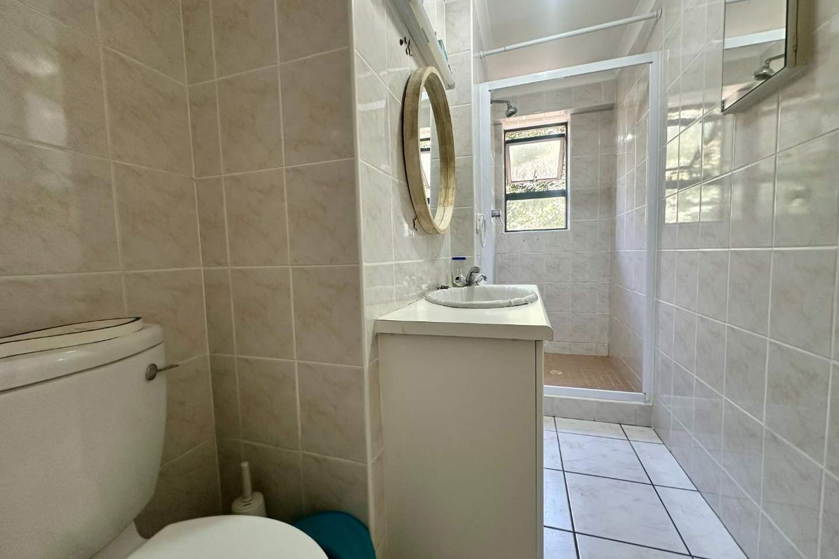 A functional bathroom featuring a walk-in shower, vanity basin, and toilet with neutral wall tiling and tiled flooring.