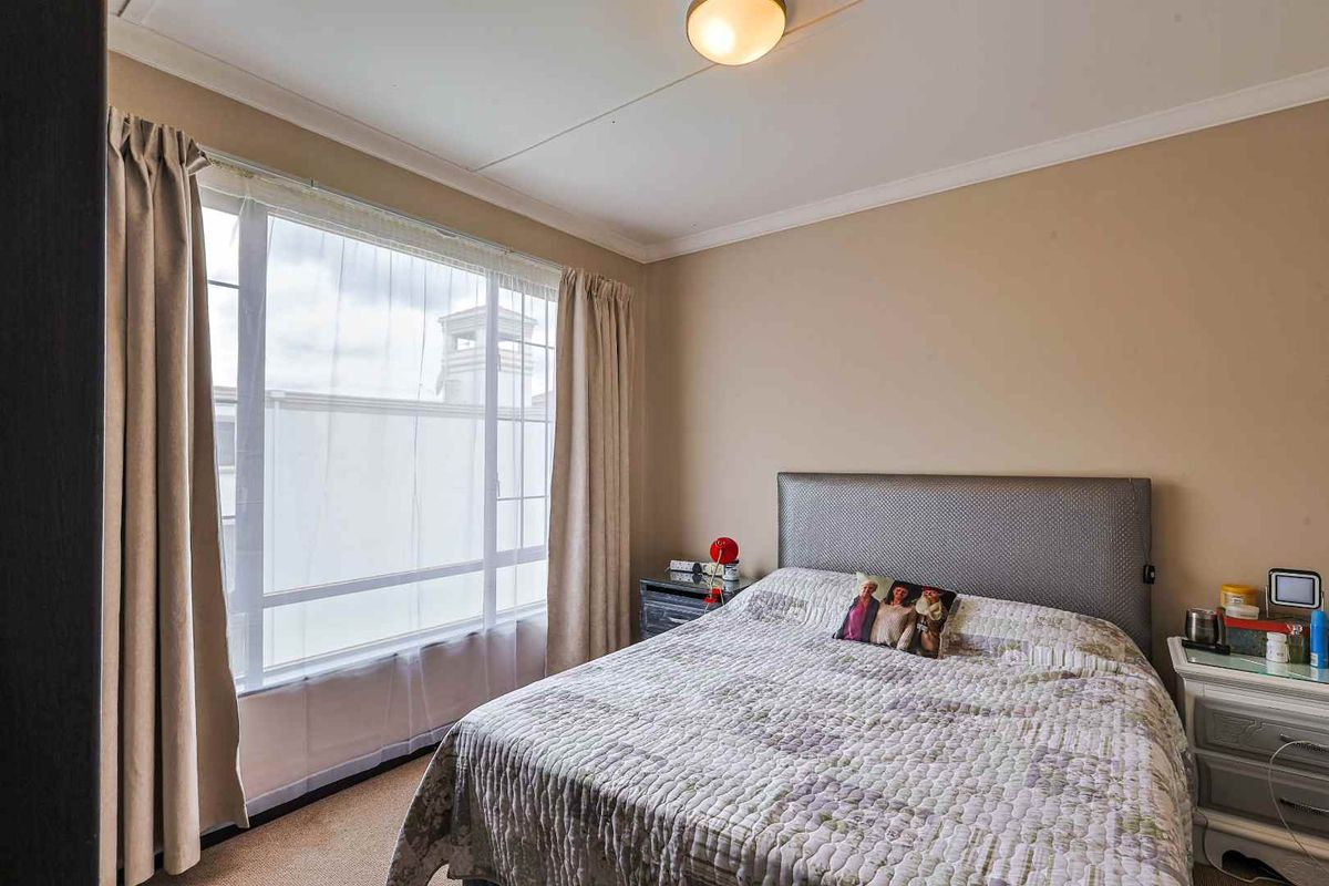 A standard bedroom featuring neutral wall tones, carpeted flooring, and a large window allowing natural light.