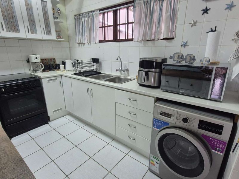 A functional kitchen featuring white cabinetry, tiled backsplash, double basin sink, and integrated laundry facilities with a freestanding stove.