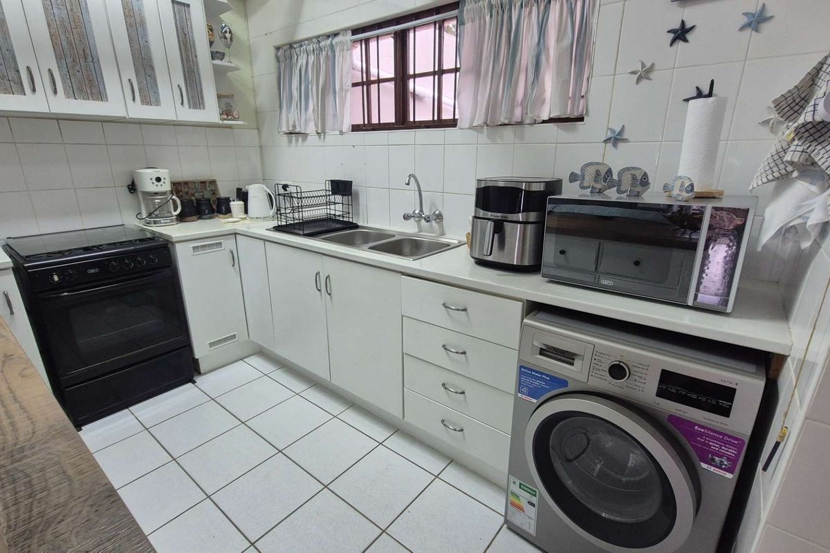 A functional kitchen featuring white cabinetry, tiled backsplash, double basin sink, and integrated laundry facilities with a freestanding stove.