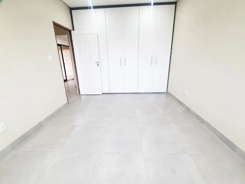 A clean, empty bedroom featuring neutral tiled flooring and modern white built-in cupboards, offering a blank canvas for personalization.