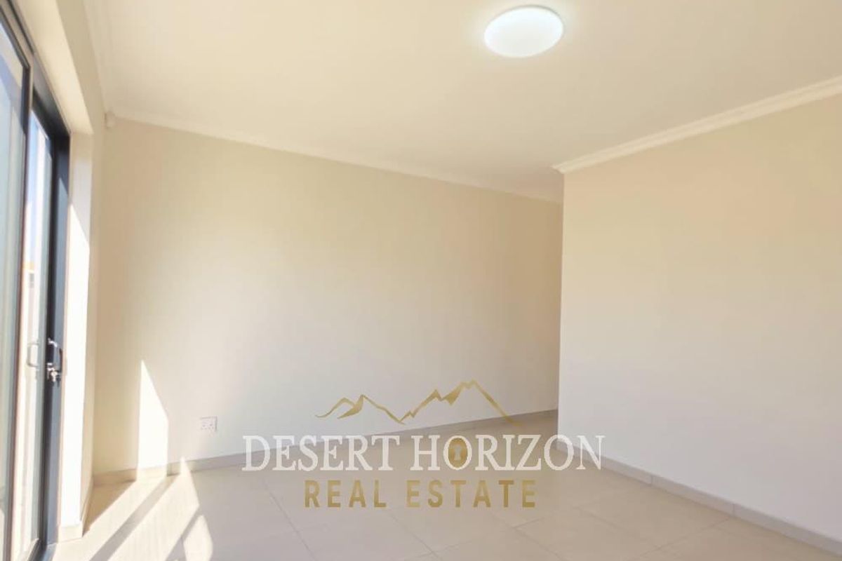 A bright, empty living area featuring neutral tiled flooring, modern ceiling lighting, and large sliding glass doors providing natural light.