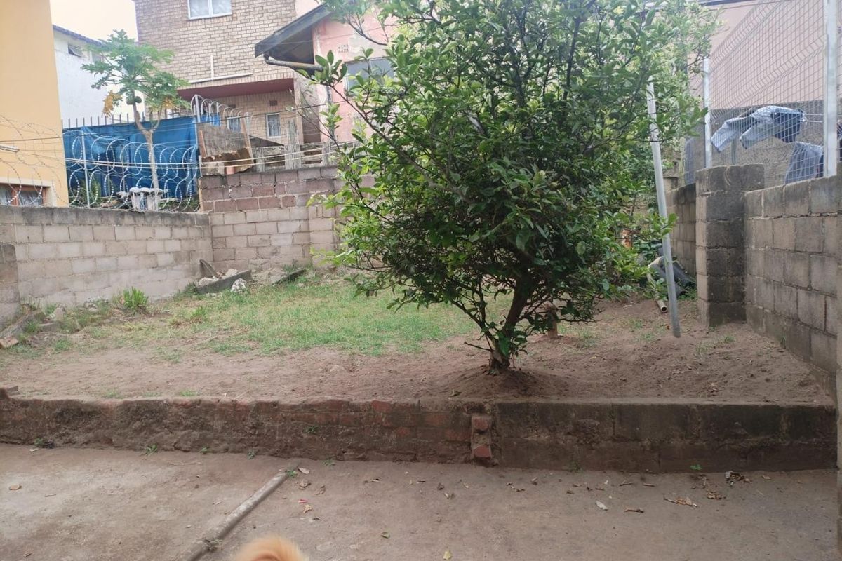 A rear garden area featuring a concrete patio, brick retaining wall, and perimeter boundary walls secured with razor wire.