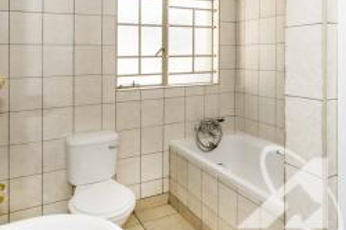 A functional bathroom featuring a standard bathtub, toilet, and tiled finishes throughout, complete with a security-barred window for ventilation.