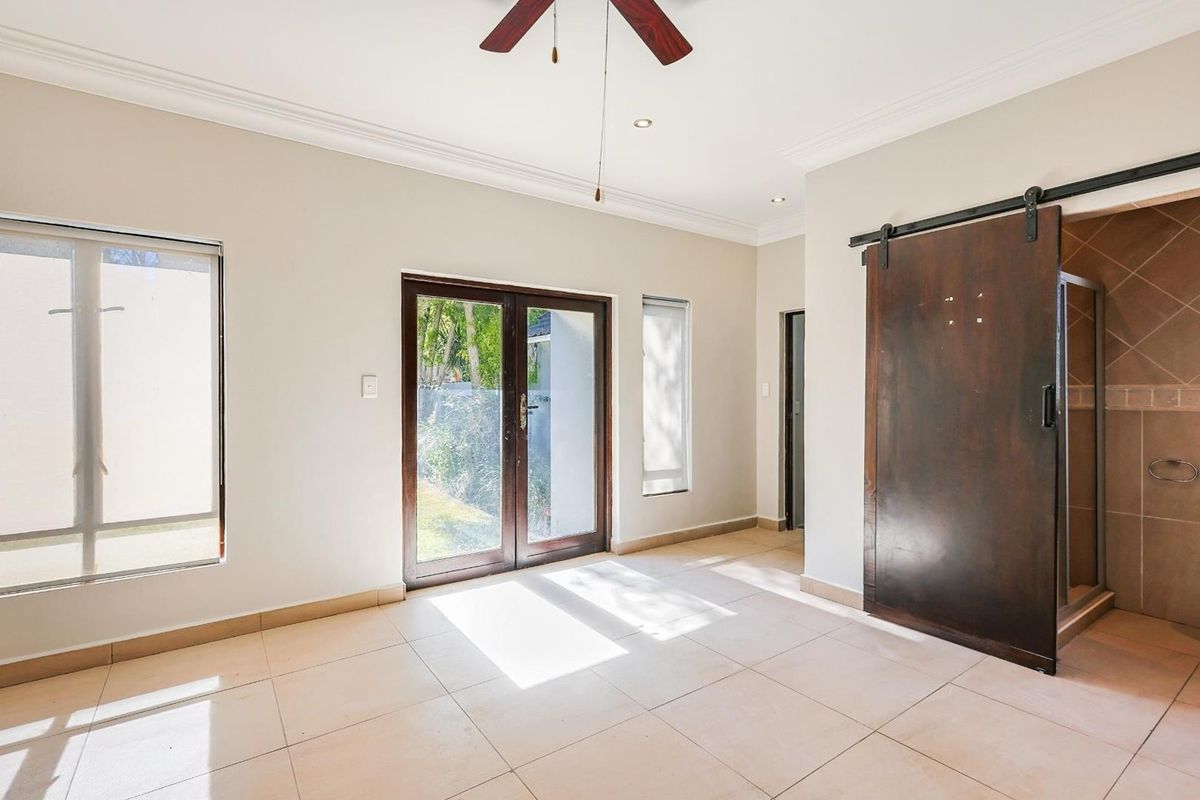 Spacious bedroom featuring tiled flooring, a ceiling fan, and a sliding barn door providing access to an en-suite bathroom with direct outdoor access.