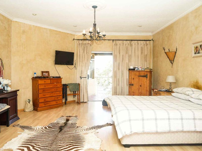 Spacious bedroom featuring laminate flooring, a ceiling rose with chandelier, and direct access to a private balcony through sliding doors.