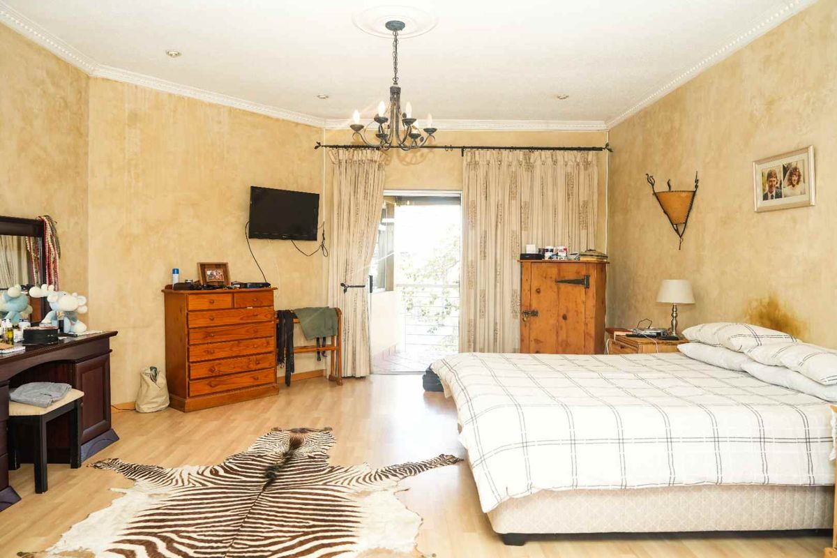 Spacious bedroom featuring laminate flooring, a ceiling rose with chandelier, and direct access to a private balcony through sliding doors.