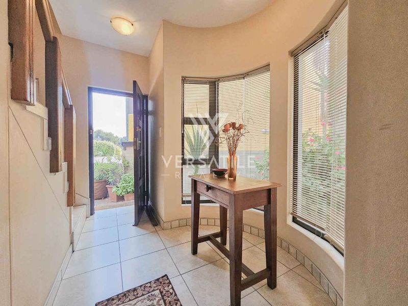 A bright entrance hall featuring tiled flooring, a staircase, and a large bay window that allows for natural light.