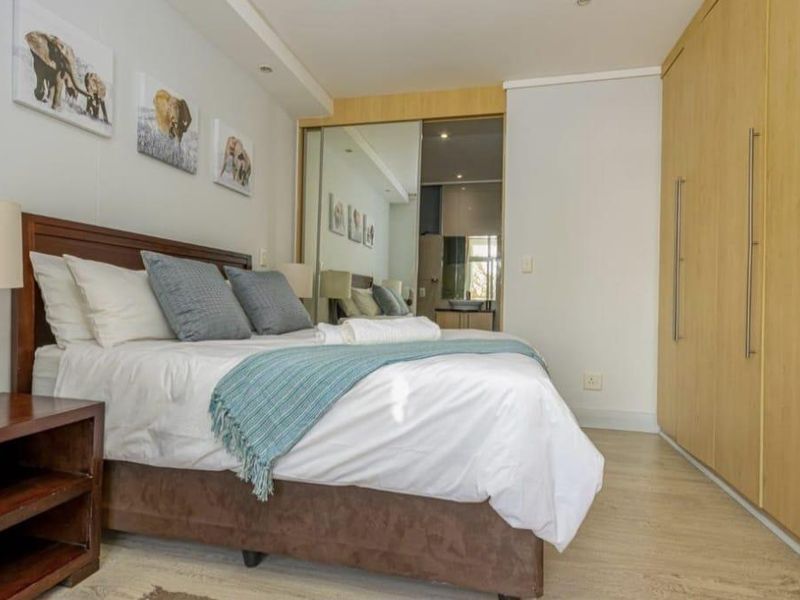 A well-maintained bedroom featuring light wood-finish built-in cupboards, laminate flooring, and mirrored sliding doors leading to an en-suite bathroom.