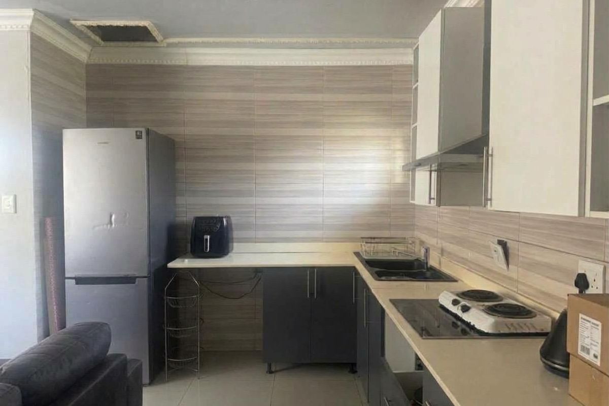 A functional kitchen featuring modern cabinetry, tiled splashbacks, a built-in hob, and an extractor fan, though the ceiling requires minor repair.