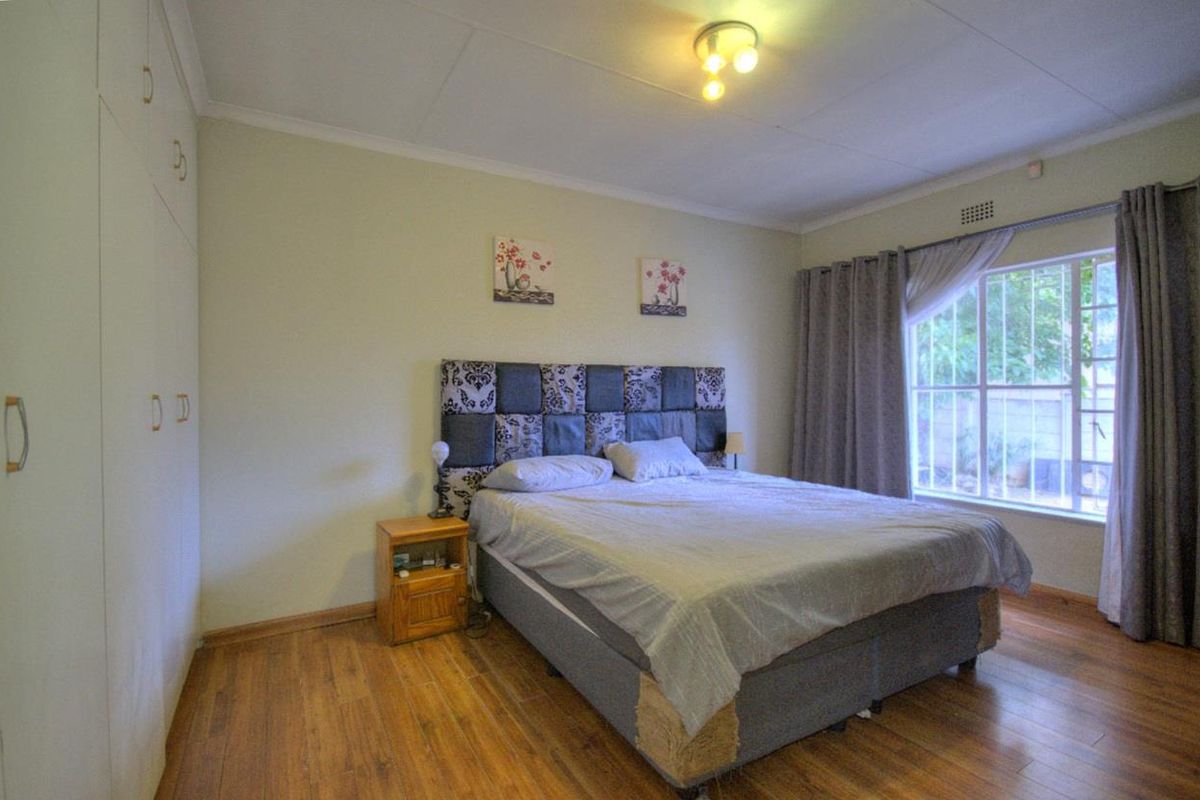 A bedroom featuring built-in cupboards, wood-look flooring, and a window with security bars, providing a functional and comfortable sleeping space.
