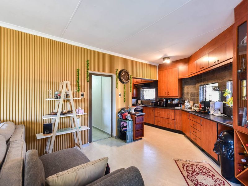 Open-plan kitchen and living area featuring warm-toned wooden cabinetry, dark countertops, and a textured feature wall.