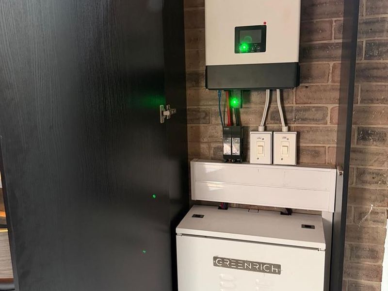 A dedicated utility space featuring a modern solar inverter and lithium battery storage system neatly installed against a brick wall.