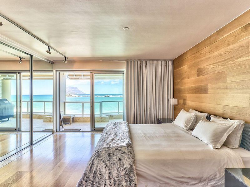 Spacious bedroom featuring hardwood flooring, a wood panel feature wall, mirrored wardrobes, and sliding glass doors opening to a balcony with ocean views.